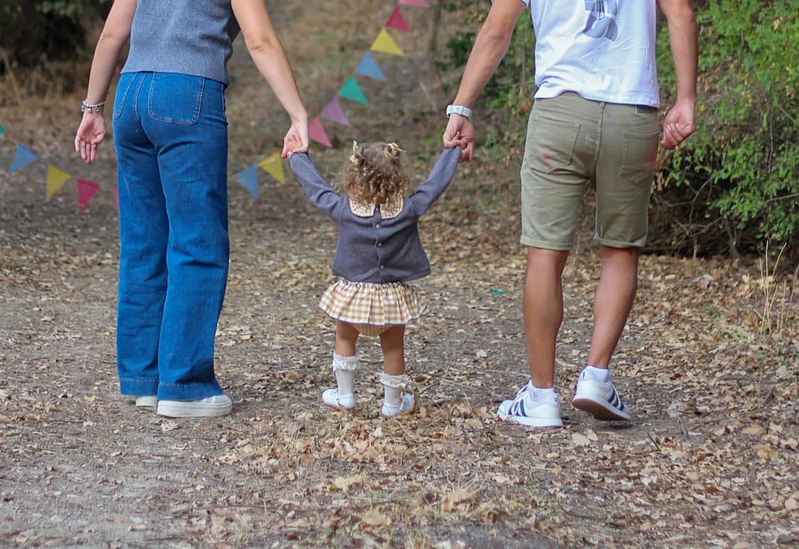 Familia caminando de la mano por un sendero, acompañando a una niña pequeña