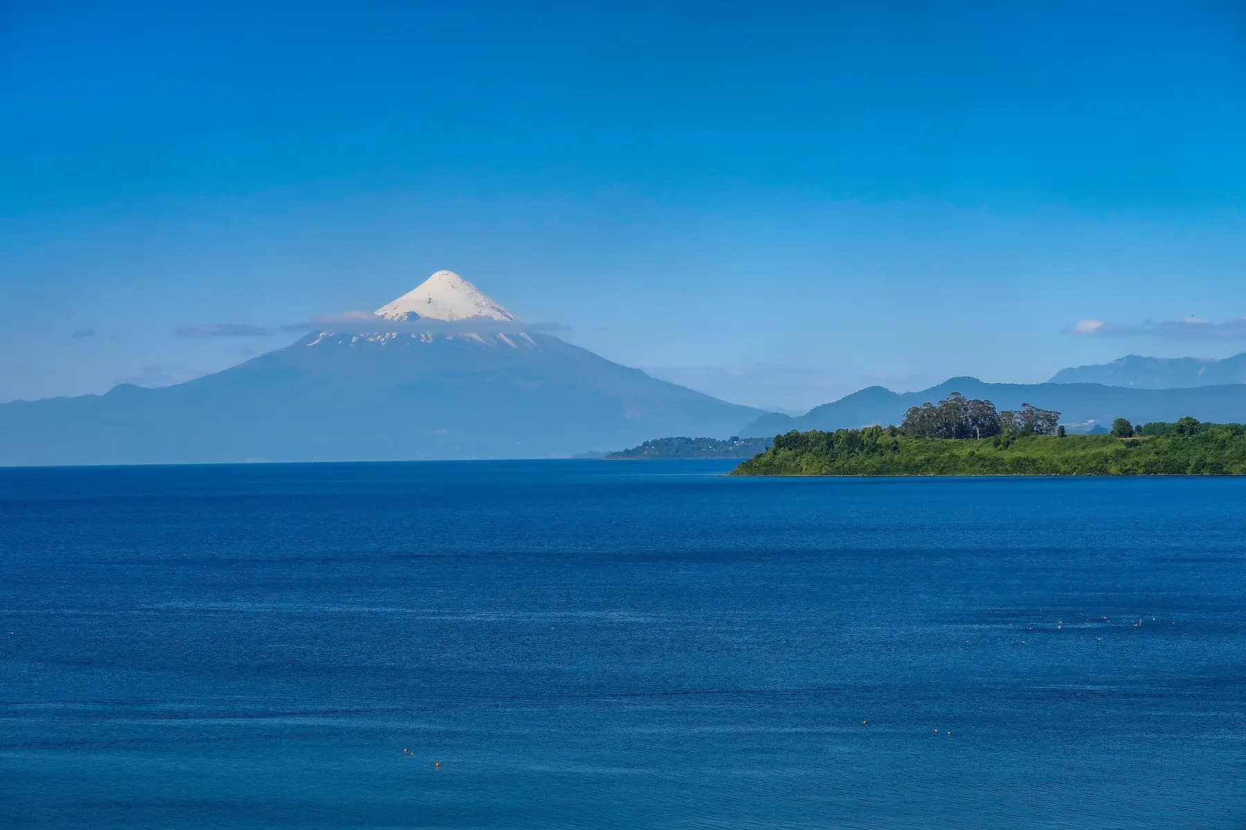 Volcán Osorno nevado bajo un cielo despejado sobre las aguas azul profundo del lago Llanquihue