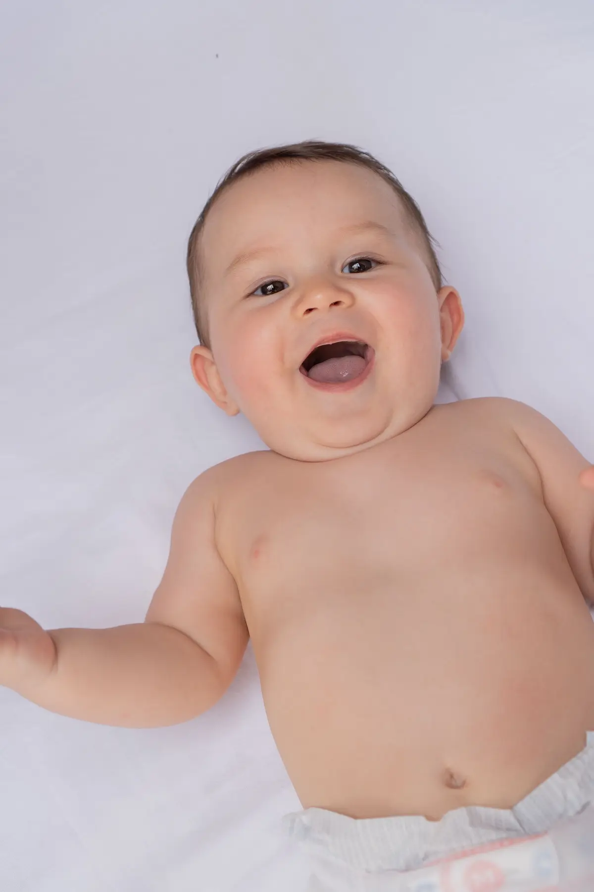 Bebé sonriendo recostado sobre una sábana blanca